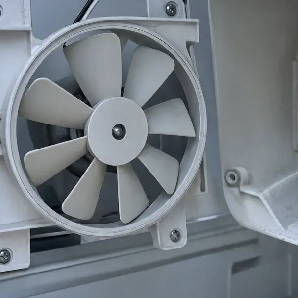 Close view of a white multi-blade fan inside its round plastic shroud.